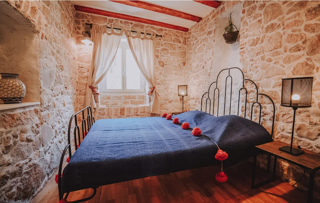 Un dormitorio con una cama cubierta con ropa de cama azul oscuro y paredes de piedra.