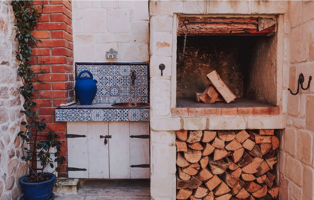 Una chimenea rústica al aire libre con leña apilada y azulejos estampados azules y blancos.