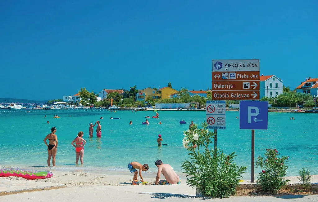 Una playa con bañistas en aguas turquesas y señales direccionales junto a la orilla.
