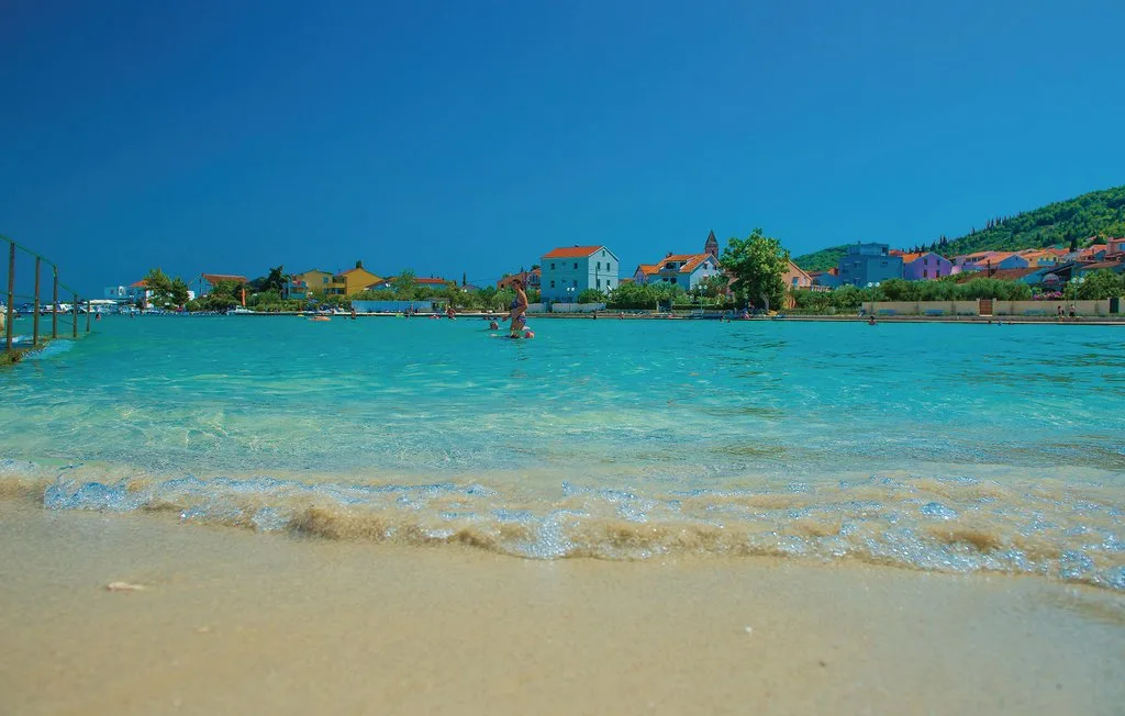 Una playa de arena bordea aguas turquesas y transparentes, con edificios al otro lado de la bahía.