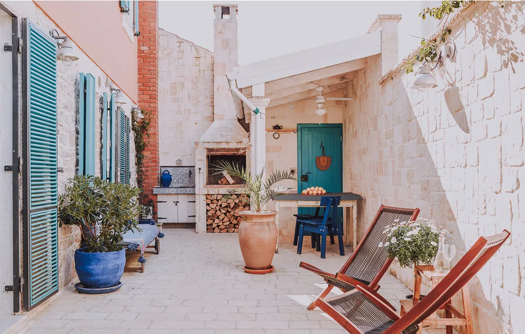 Un patio de piedra con asientos al aire libre, plantas en macetas y un comedor cubierto.