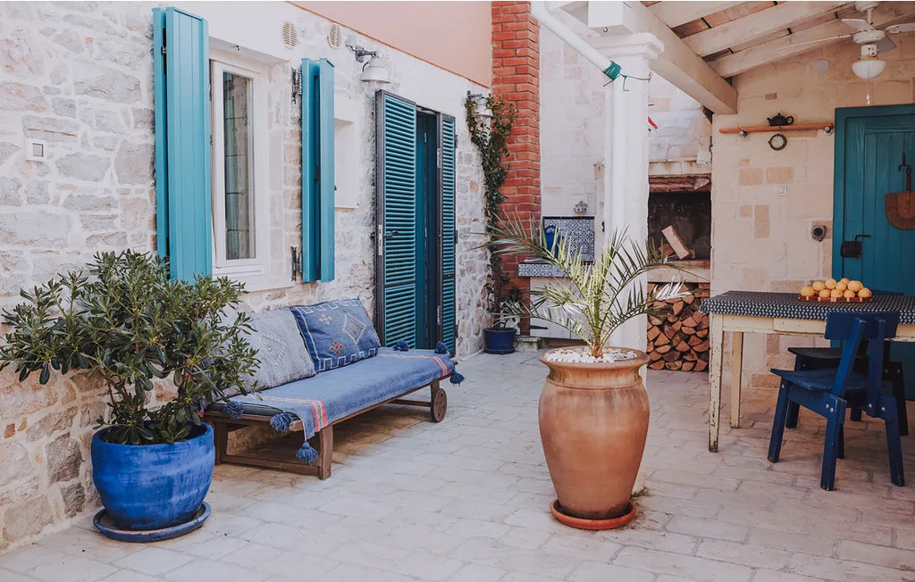 Un patio de piedra con contraventanas azules, asientos al aire libre y plantas en macetas.