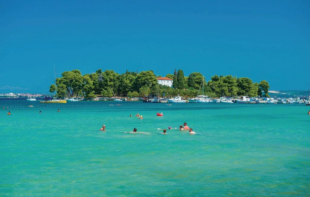 Una bahía turquesa con bañistas en primer plano y una isla cubierta de árboles al fondo.