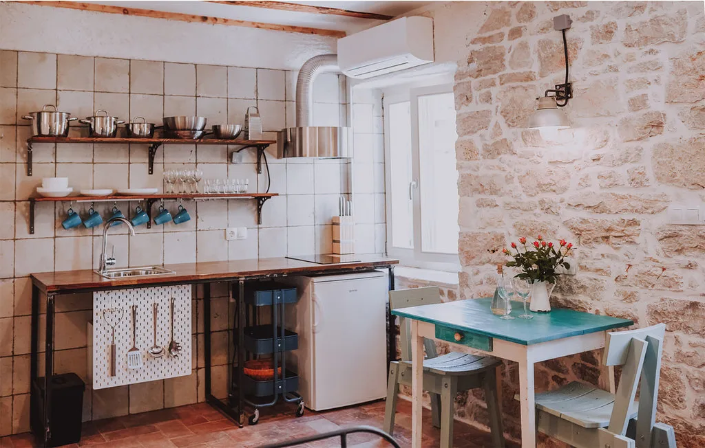 Una cocina con encimeras de azulejos, estantes abiertos y una pequeña mesa de comedor.