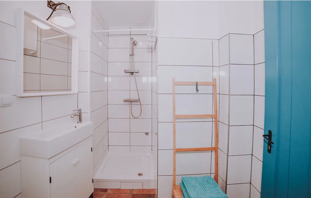 Un baño alicatado con lavabo, ducha y toallero de madera.