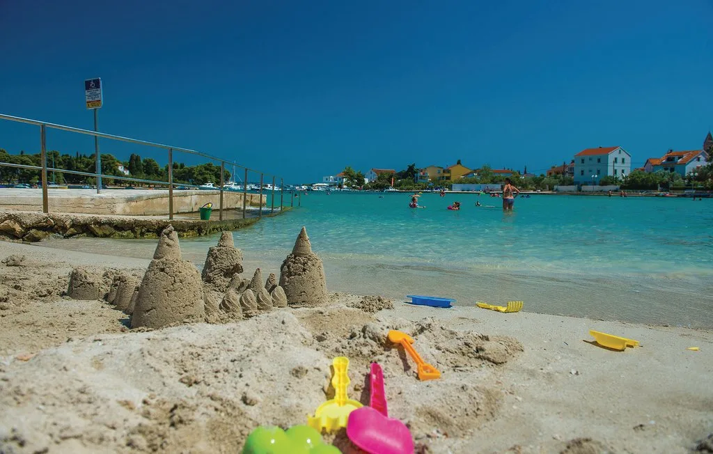 Una playa de arena con castillos, juguetes de colores y agua turquesa clara.