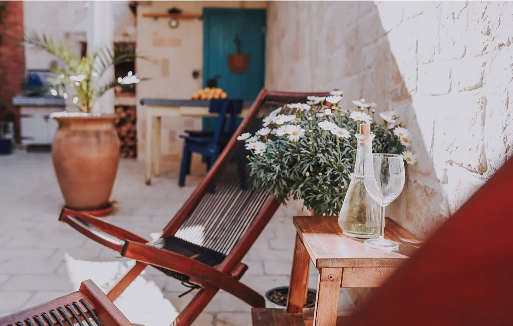 Una zona de estar en un patio con una silla de madera, flores y una mesa pequeña.