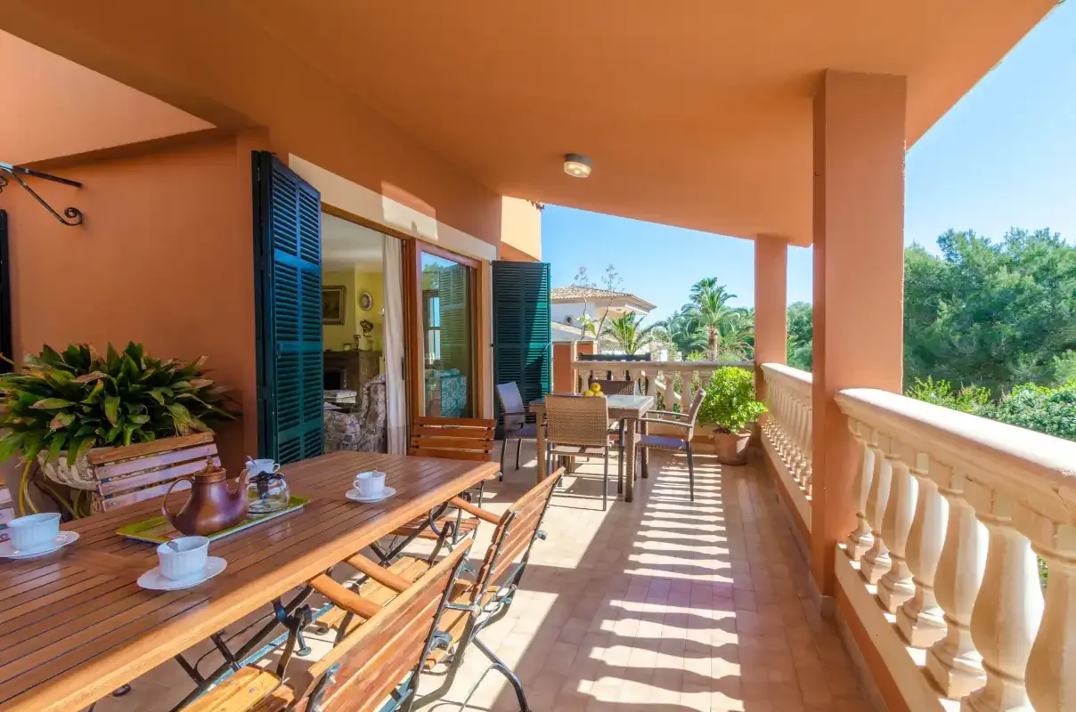 Un patio cubierto con asientos y una mesa al aire libre da a una zona verde.