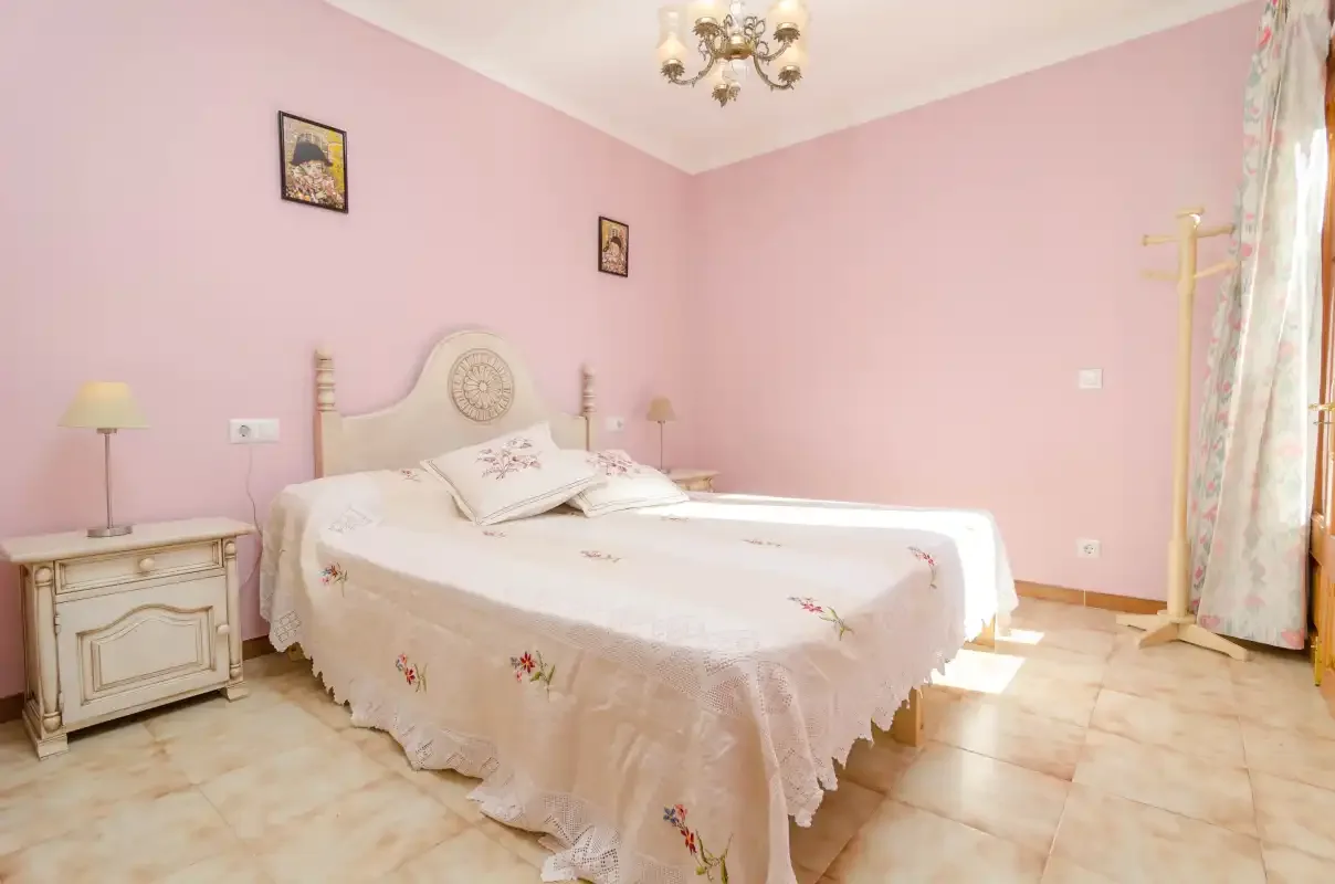 Un dormitorio con una cama, mesillas y paredes rosas.