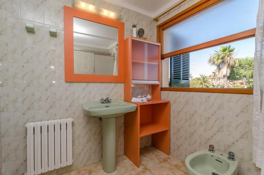 Un baño alicatado con lavabo, espejo y una ventana con vistas a palmeras.