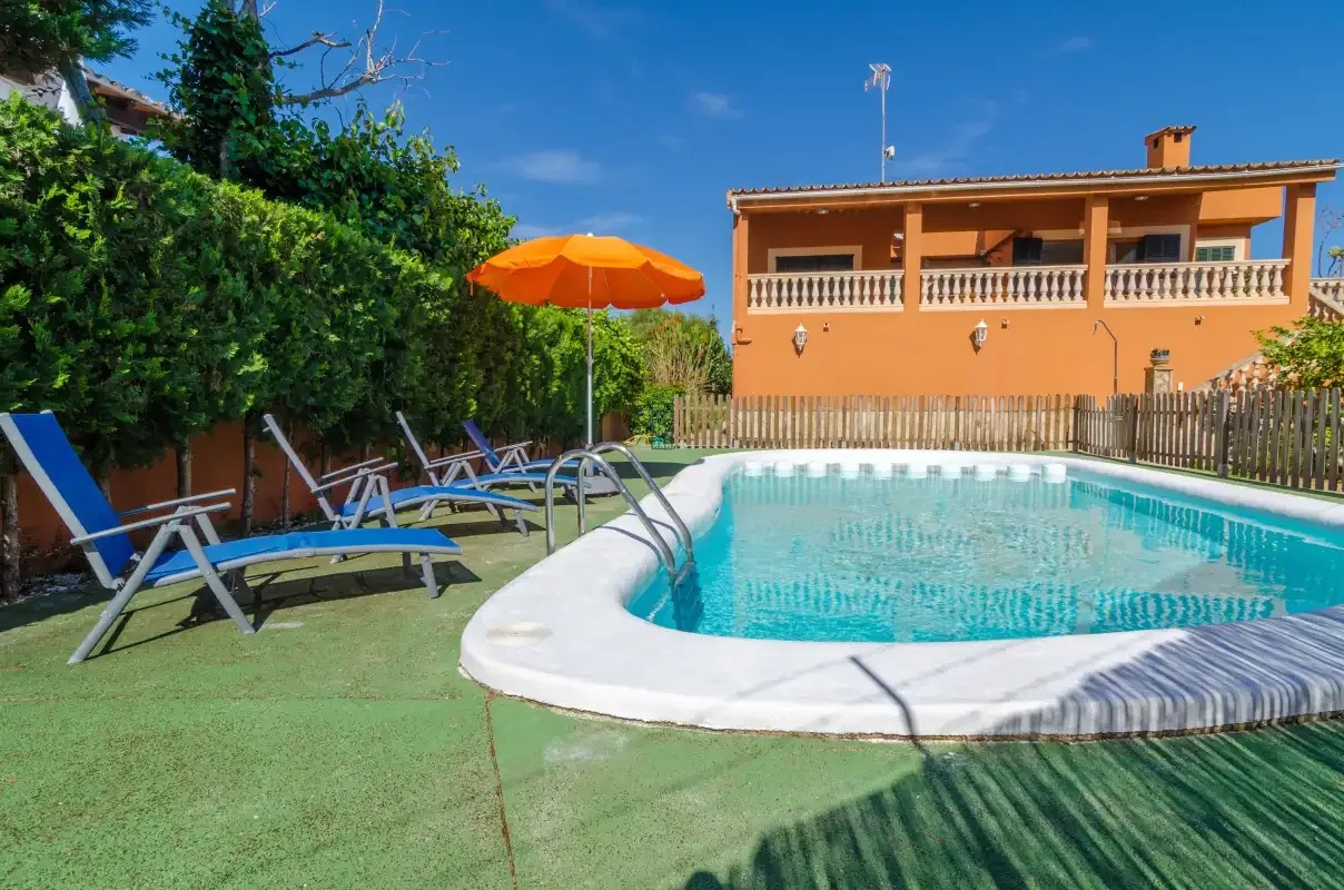 Una piscina al aire libre está junto a asientos reclinables y un edificio de dos plantas.