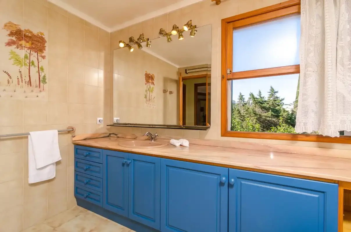 Un baño luminoso con un largo mueble de lavabo, espejo y ventana.