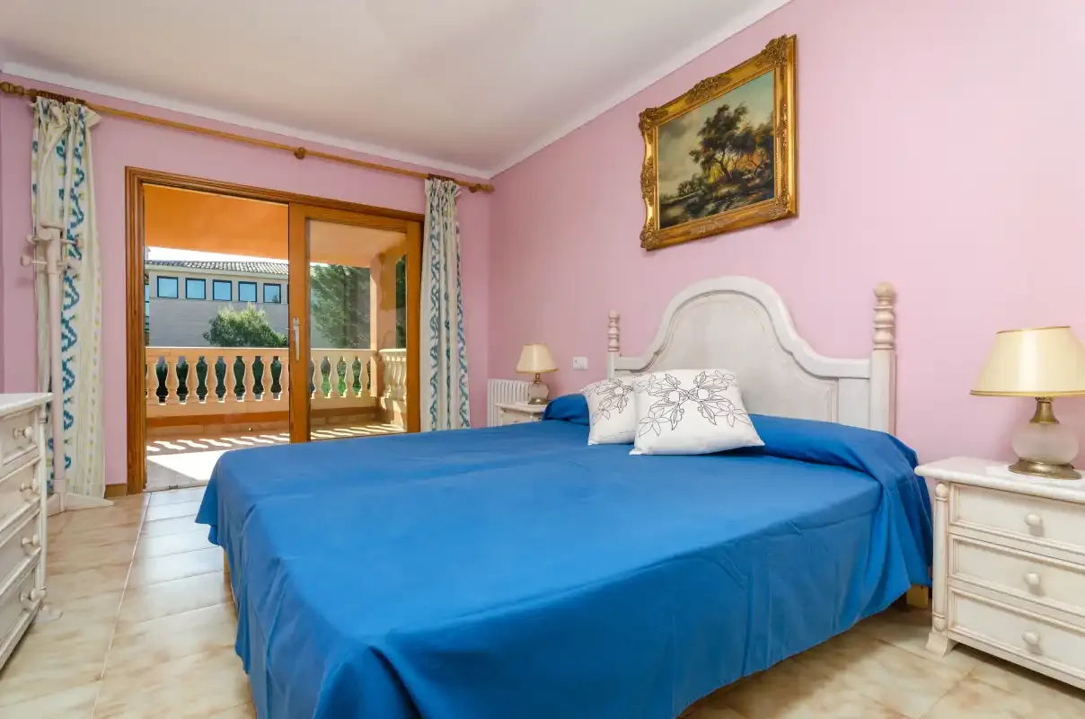 Un dormitorio con una cama cubierta de azul y puertas de cristal que dan a un balcón.