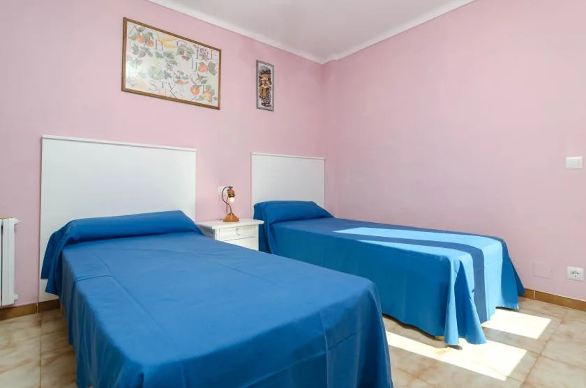 Un dormitorio rosa con dos camas azules y cuadros en la pared.