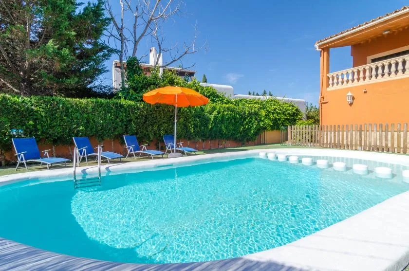 Una piscina al aire libre junto a un seto, con tumbonas y una sombrilla naranja.