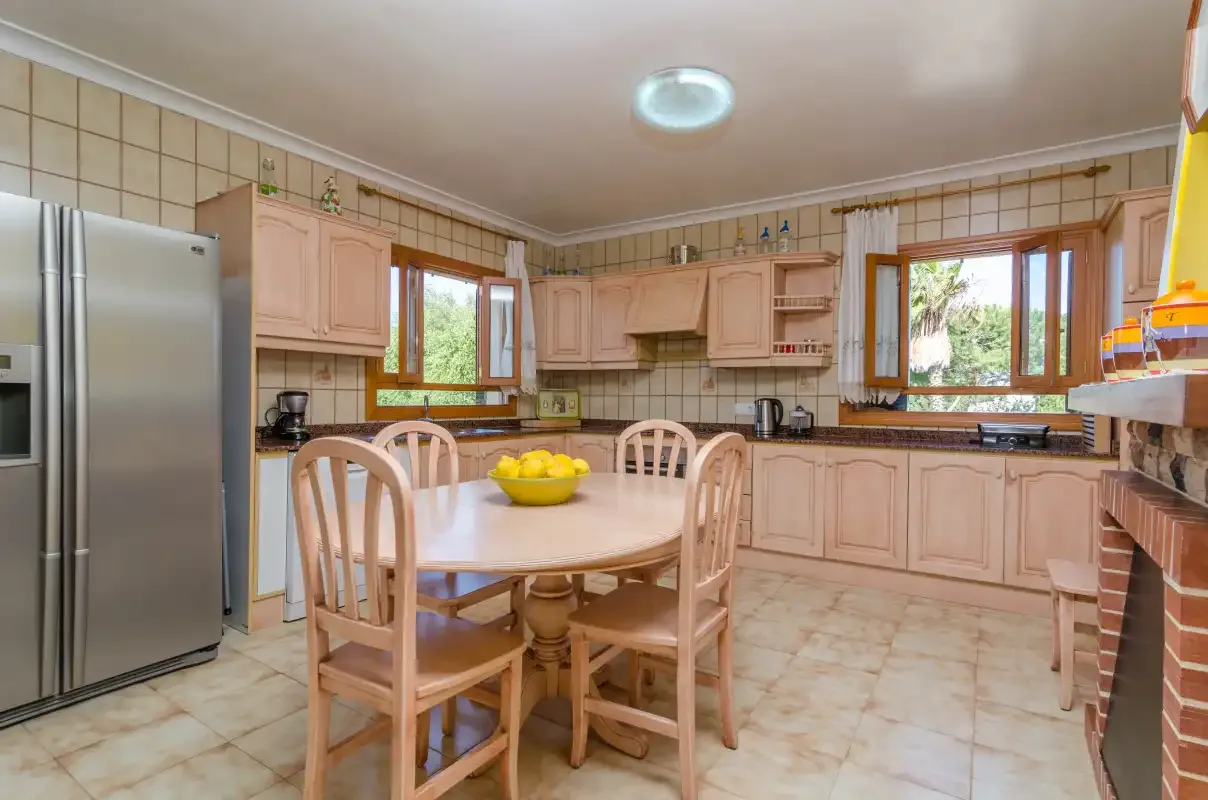 Cocina y comedor con azulejos, armarios de madera y una mesa.