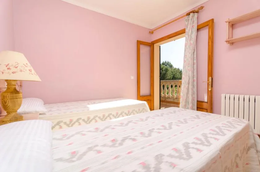 Un dormitorio rosa con dos camas y una puerta abierta al balcón.