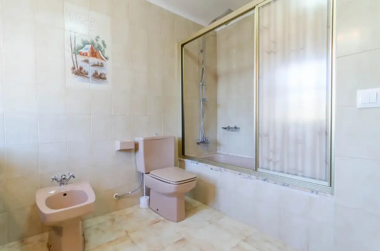 Un baño con azulejos, inodoro, lavabo y ducha con mampara de vidrio.