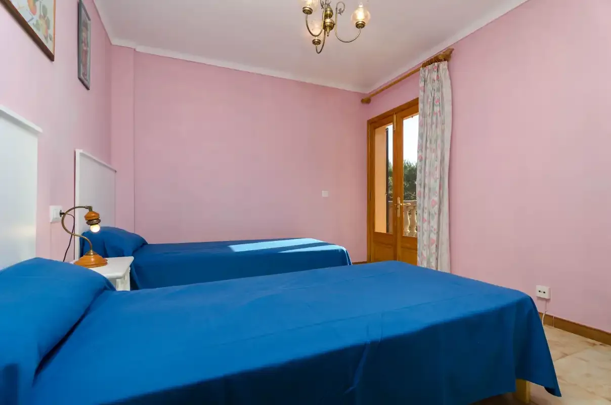 Un dormitorio rosa con camas cubiertas de azul y una puerta acristalada con marco de madera.