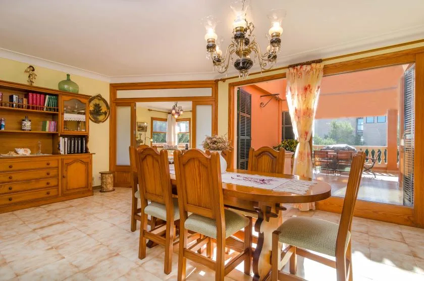 Un comedor con una mesa de madera y asientos junto a una gran puerta de vidrio.