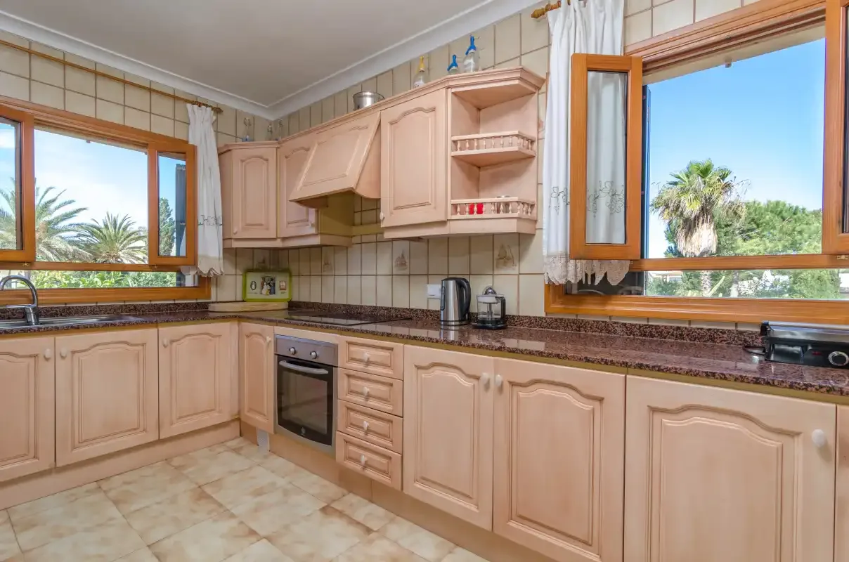 Una cocina luminosa con armarios claros, paredes revestidas de azulejos y ventanas amplias.
