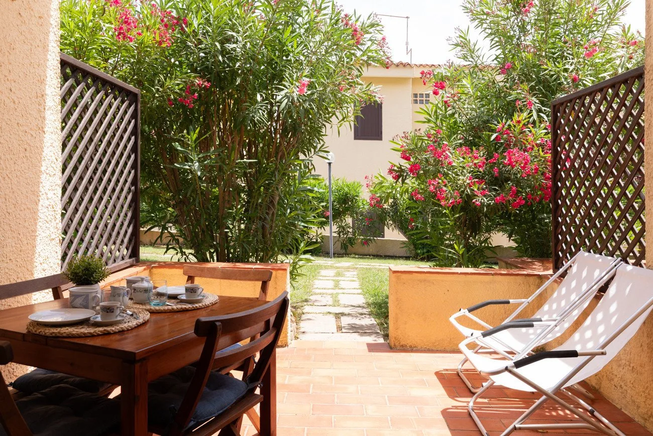 A garden patio with outdoor seating, a dining table, and flowering shrubs.