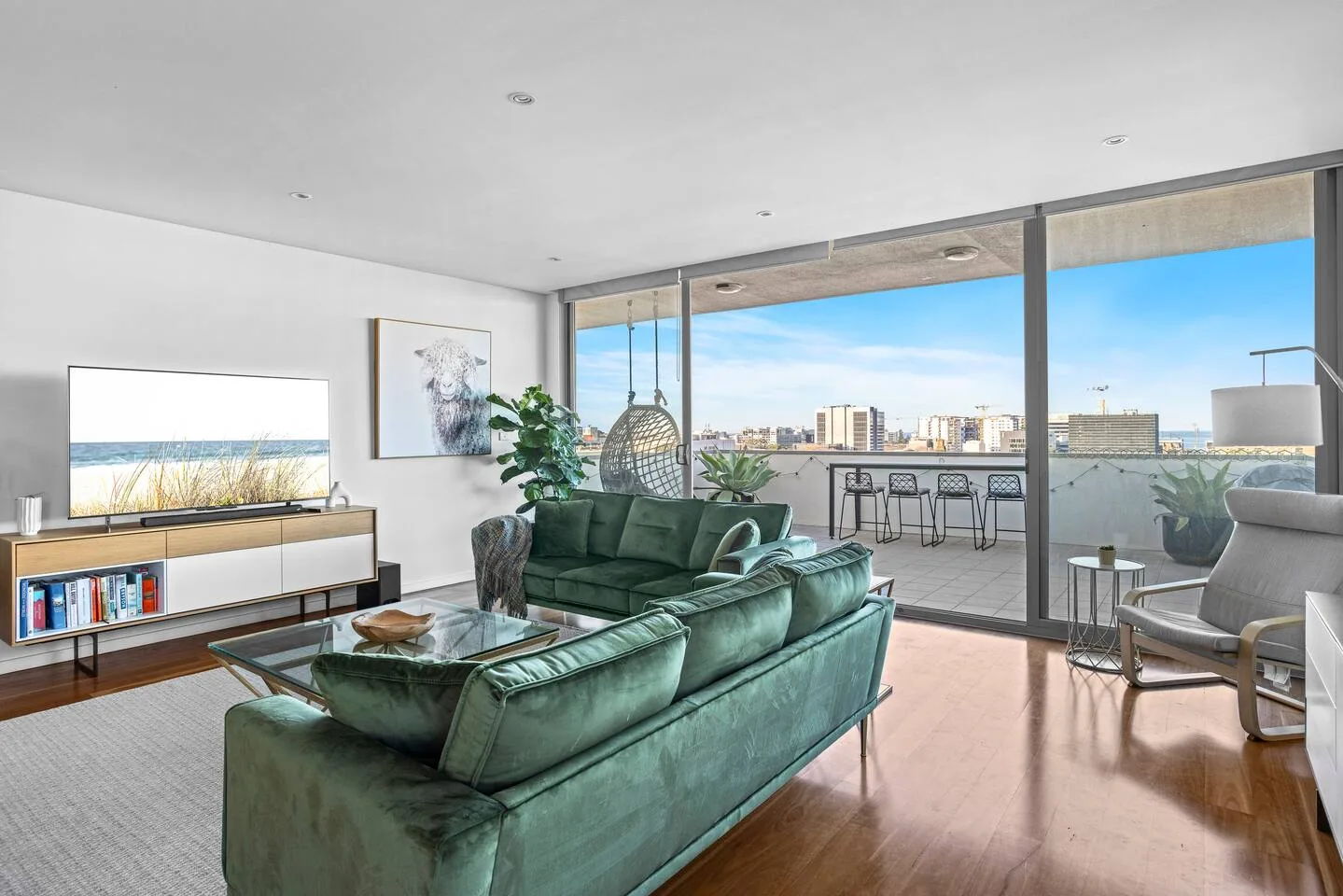 A living room opens onto a balcony through broad glass doors, with green seating facing the view.