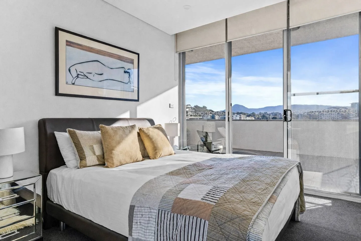 A bedroom with a bed beside floor-to-ceiling windows overlooking a balcony.