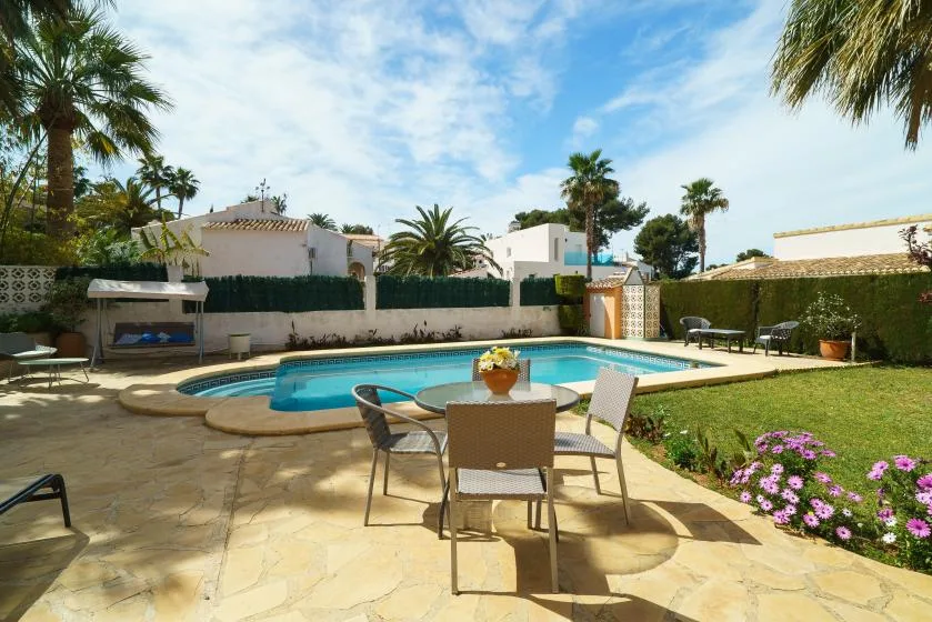 A sunny outdoor pool area with a paved patio and dining table.