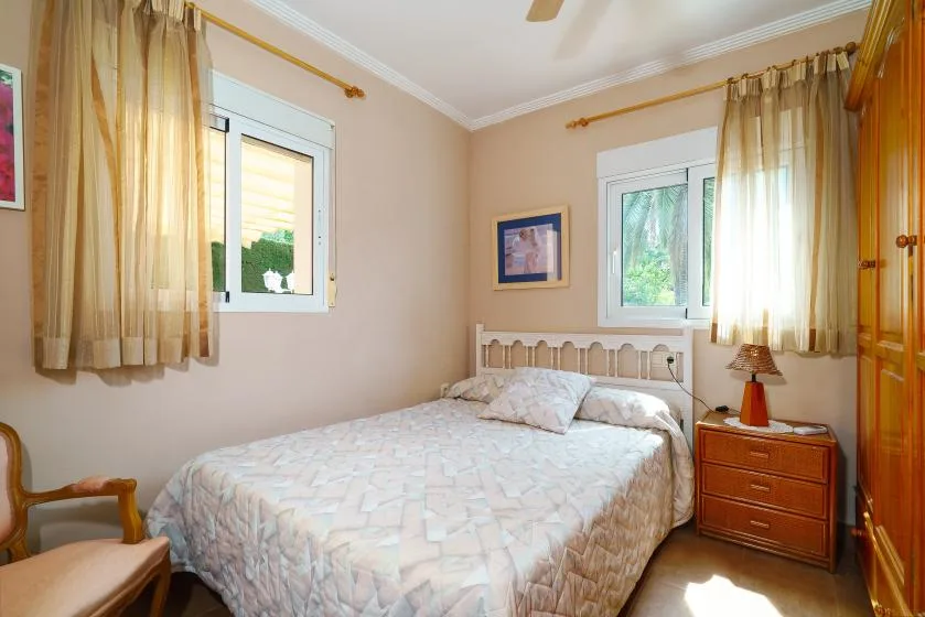 A bedroom with a bed, curtained windows, and a wooden dresser.