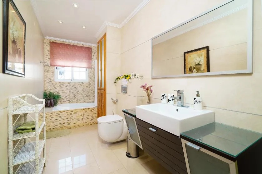 A bright bathroom with a vanity, wall mirror, and bathtub.