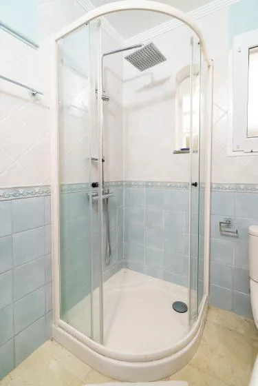 A tiled bathroom with a curved glass shower and a small window.