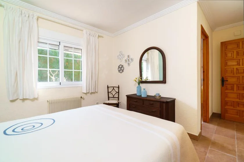 A bedroom with a bed, a window, and a dresser topped by a mirror.