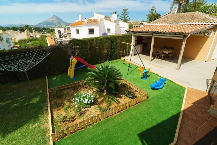 A landscaped garden with a lawn, play equipment, and a covered patio.