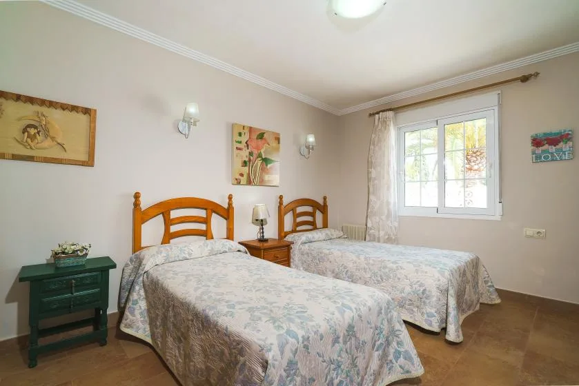 A bedroom with two beds beside a window and bedside table.