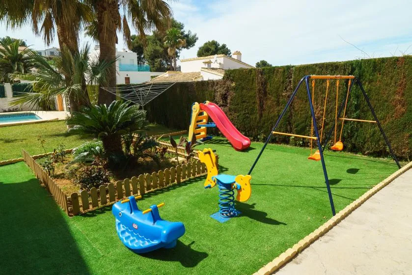 A children’s play area with a slide and swings on green turf.