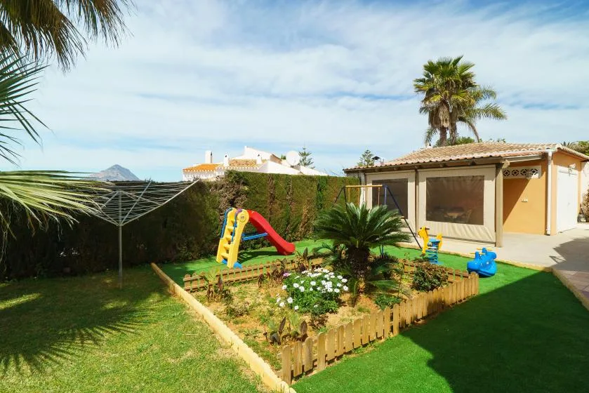 A sunny garden with a small play area, lawn, and covered patio.