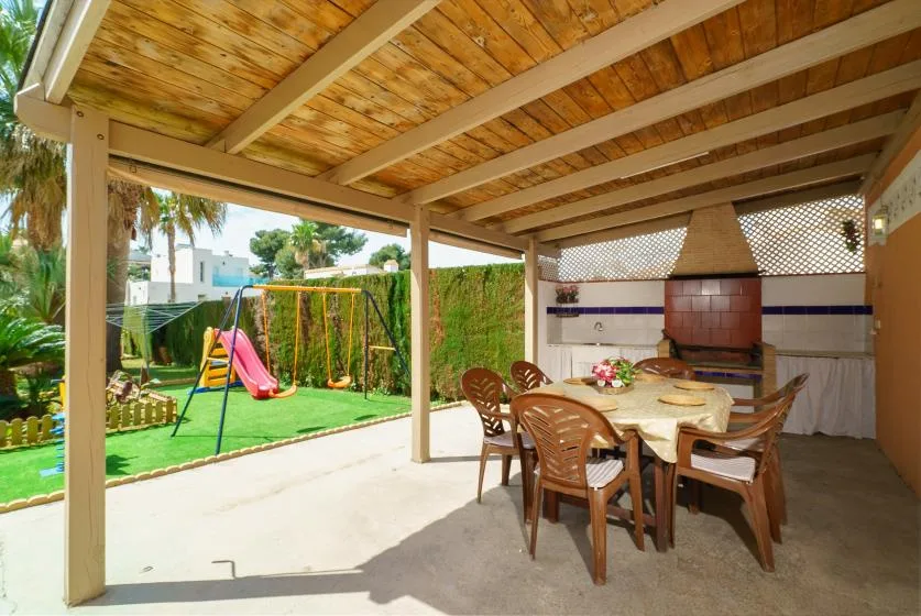 A covered outdoor dining area opens onto a garden with a children’s slide.