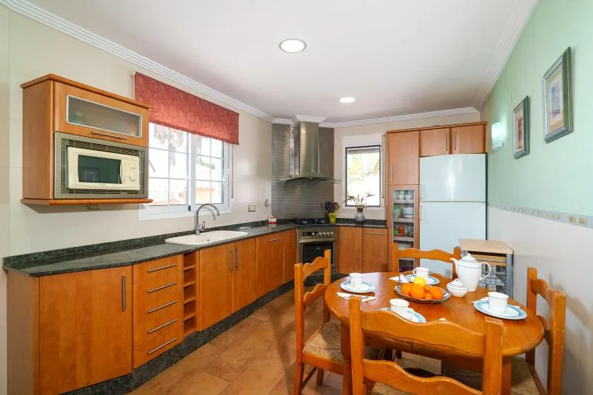 A kitchen with wooden cabinets, a cooking area, and a dining table.