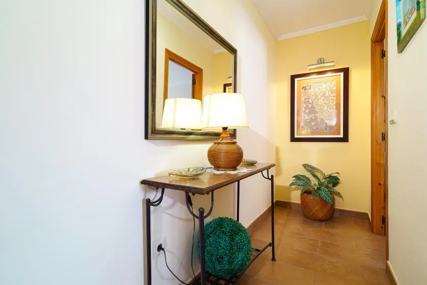 A hallway features a narrow console table, a large mirror, and framed artwork.