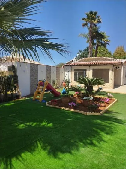 A sunny garden with a green lawn, flower bed, and children’s play equipment.
