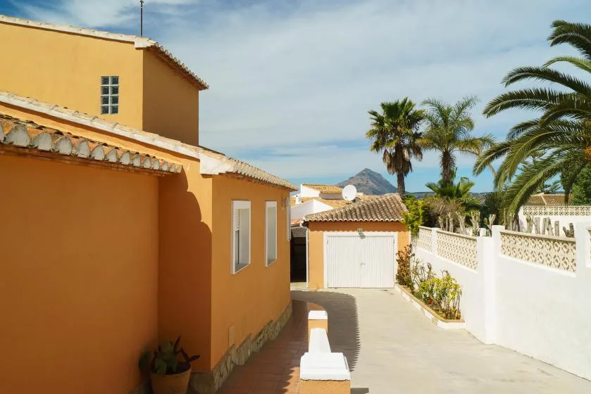 A sunny courtyard beside an orange building, with a paved path and palm trees.