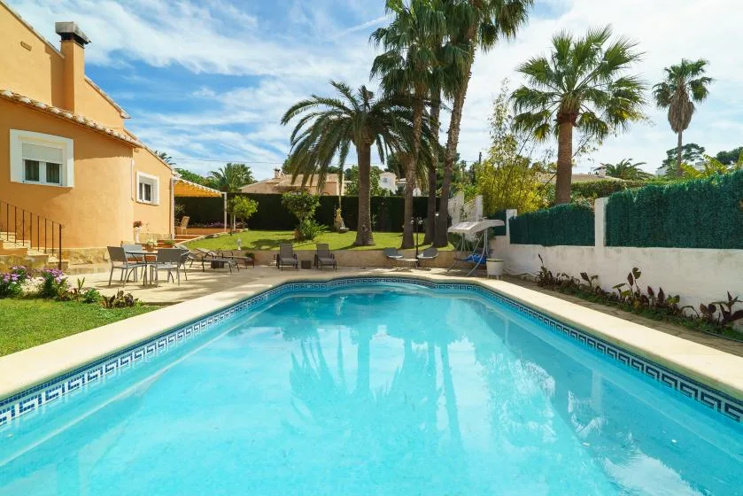 An outdoor swimming pool beside a yellow building, with palm trees and patio seating.