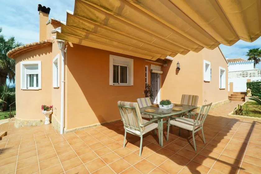 A tiled patio with a dining table and seating beneath a fabric awning.
