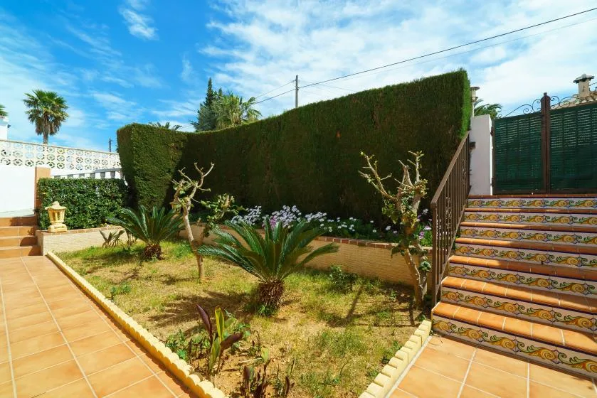 A sunny garden courtyard with tiled walkways, plants, and a staircase.