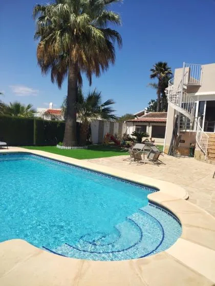 An outdoor swimming pool with curved steps sits beside a sunny patio.