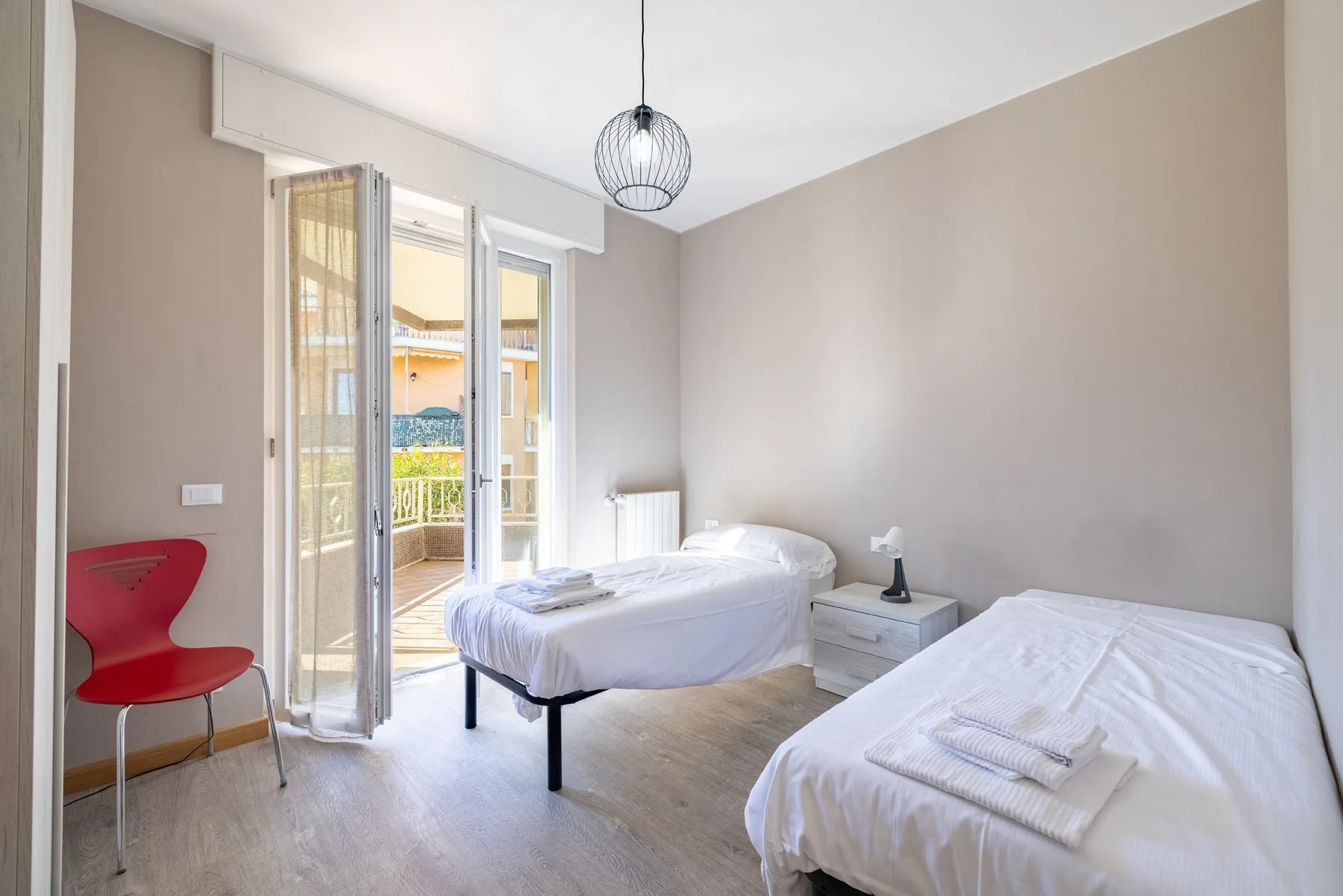 A bedroom with two beds and an open door to a balcony.