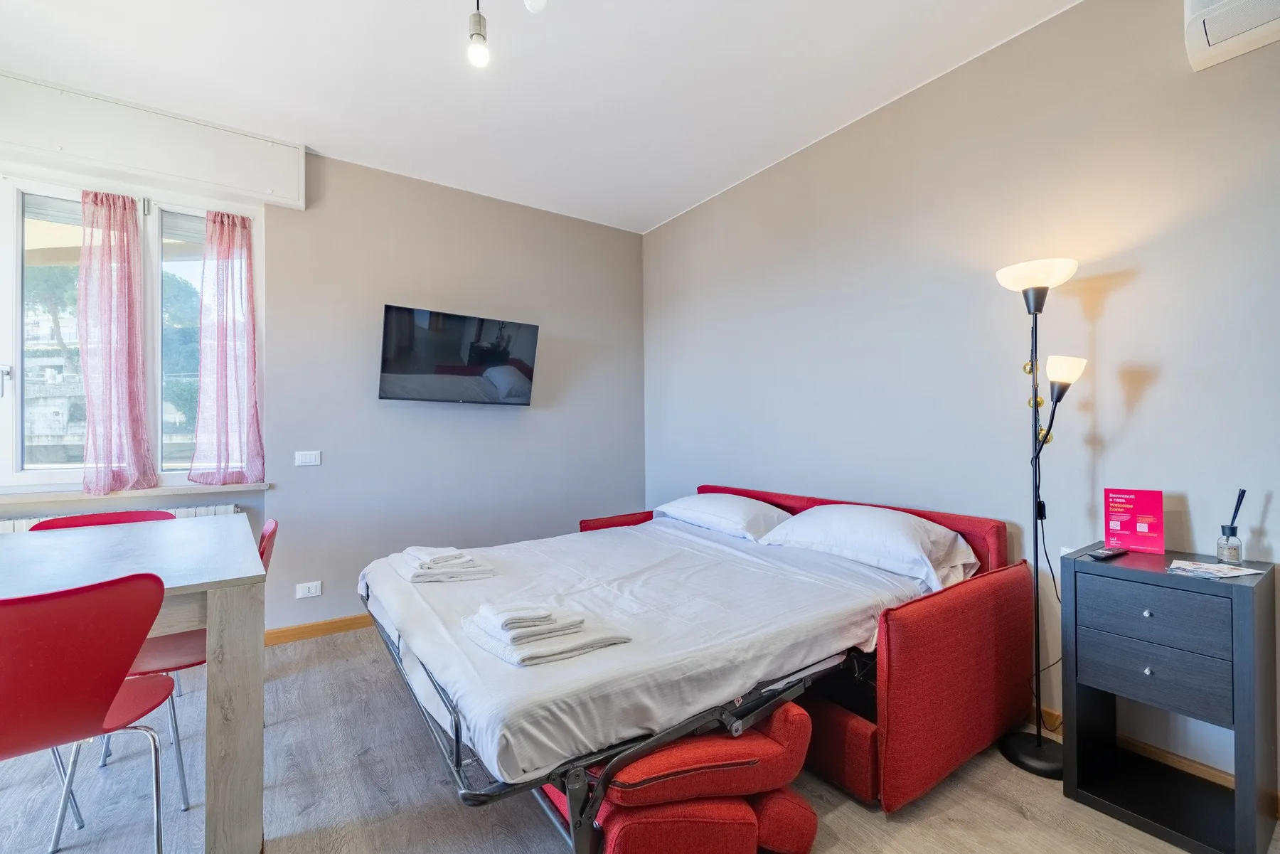A bedroom with a bed, red seating, and a wall-mounted television.