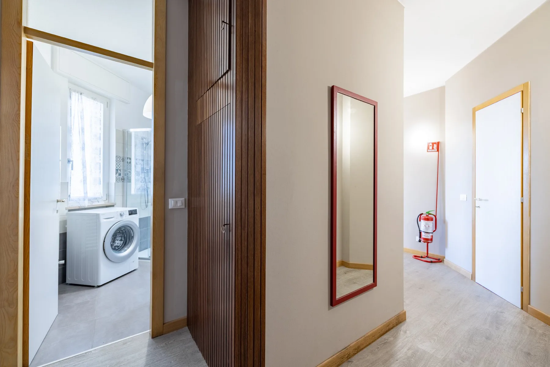 A bright hallway with a wall mirror and an open doorway to a laundry area.