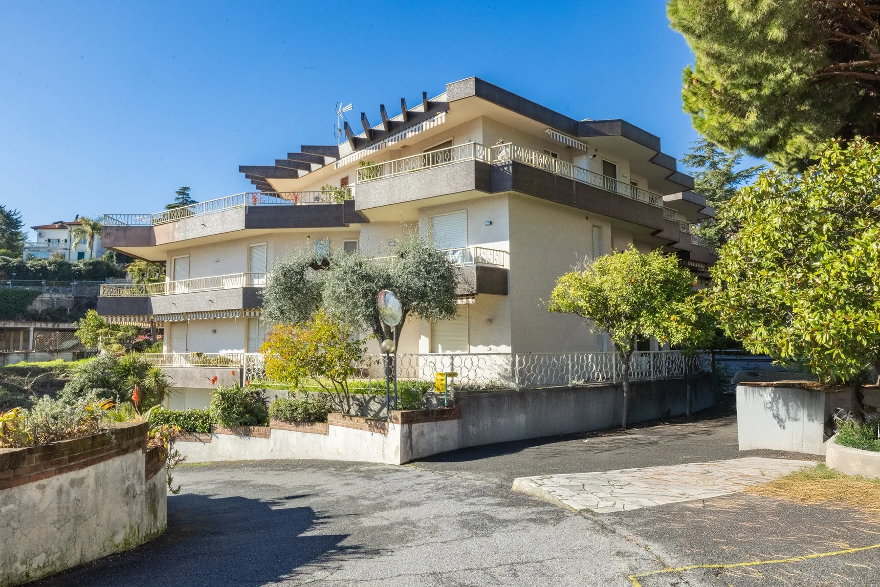 A multi-story residential building with balconies stands behind a landscaped courtyard.